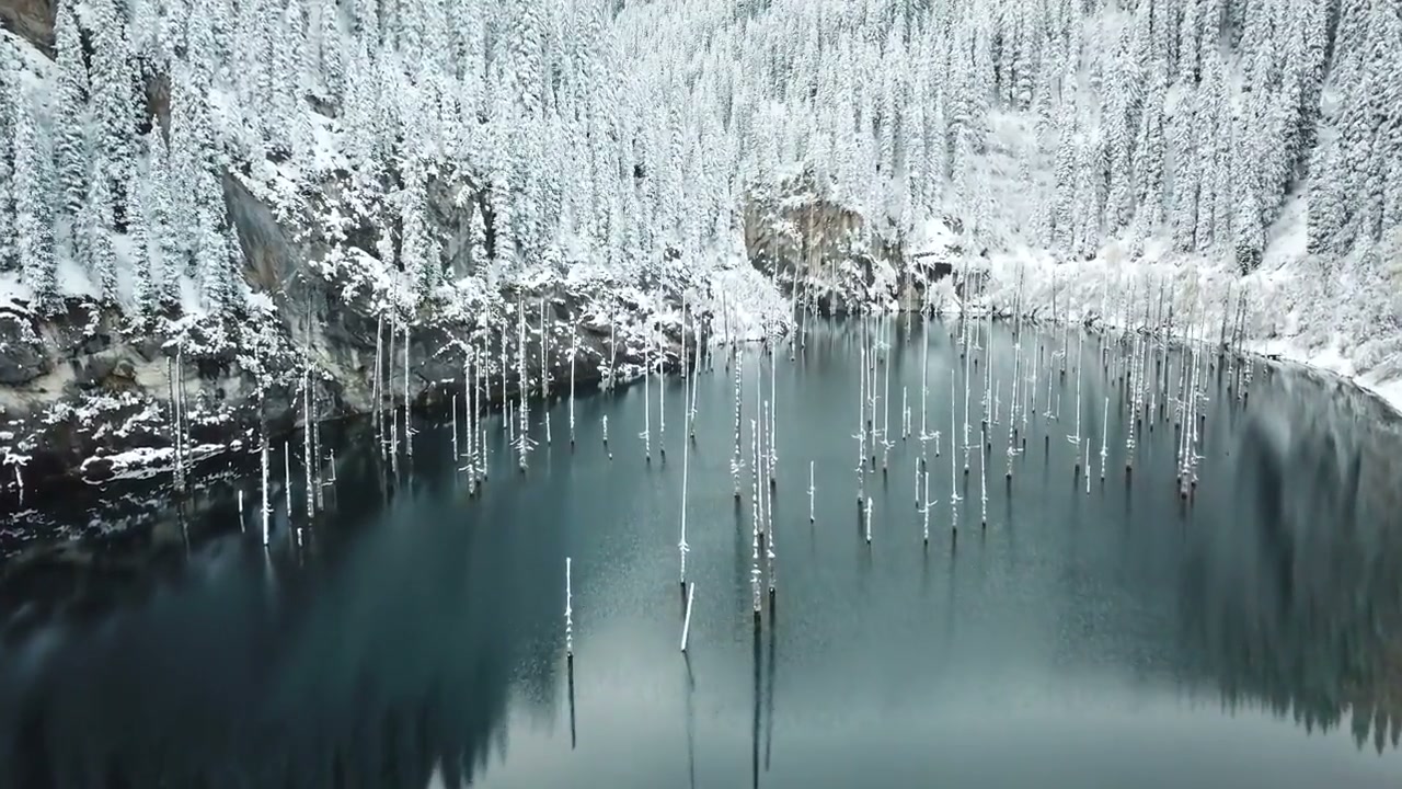 Snow-covered trees and the still water of Lake Kaindy